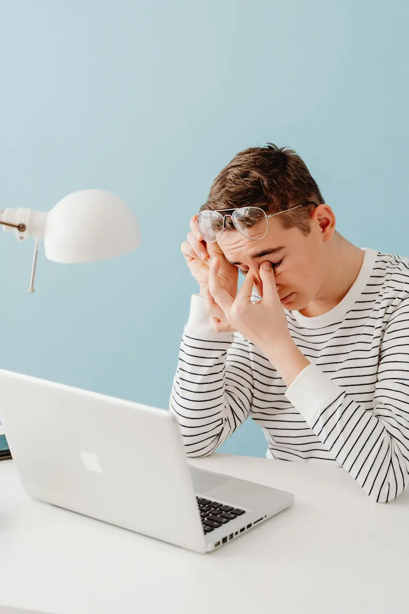stressed young man rubbing his eyes at laptop