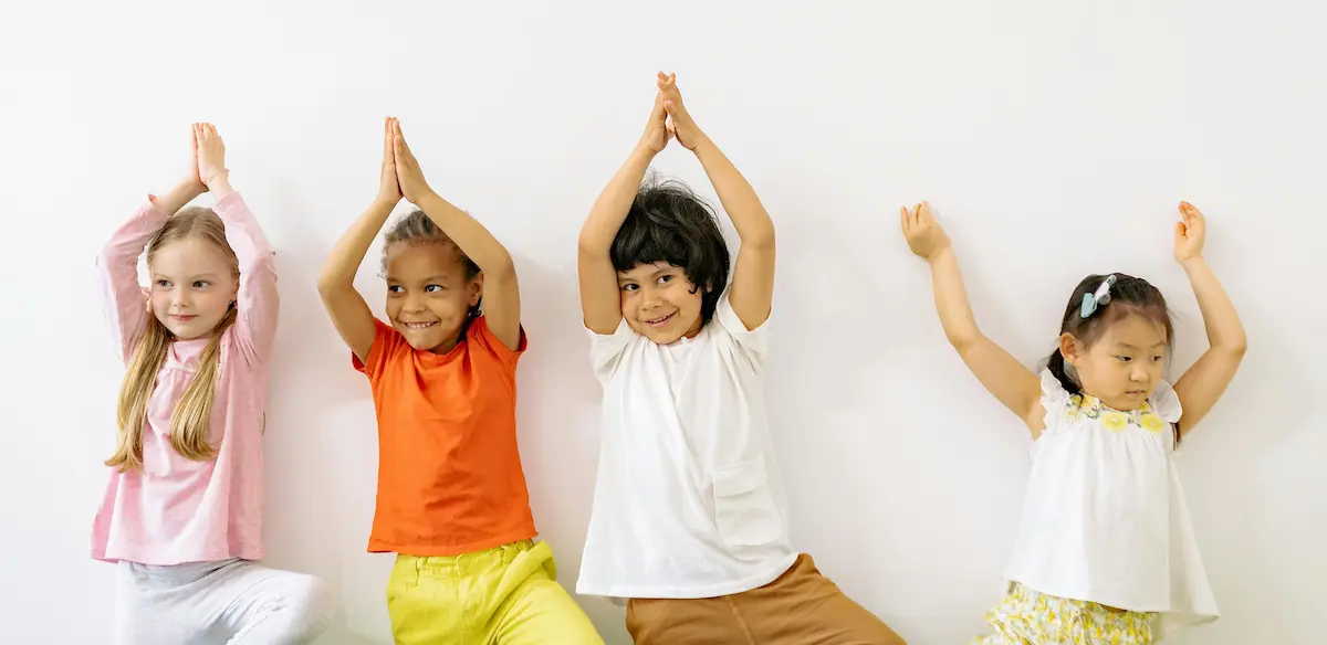 smiling children in colourful tops balancing on one leg with hands above head